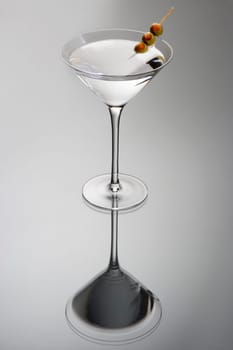 Martini mixed drink with olive garnish on a light grey background with reflection