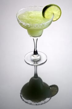 Frozen Margarita mixed drink with lime slice garnish on plain grey background with reflection