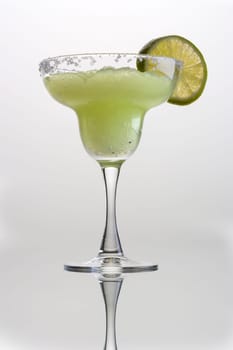 Frozen Margarita mixed drink with lime slice garnish on plain grey background with reflection