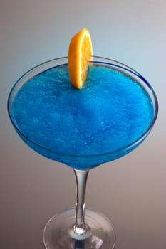 Frozen Blue Hawaiian mixed drink with orange slice garnish on grey background with reflection