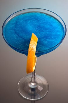 Frozen Blue Hawaiian mixed drink with orange slice garnish on grey background with reflection