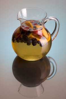 Pitcher of white wine sangria on grey background with reflection