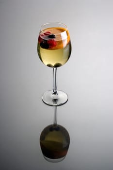 Glass of white wine sangria on grey background with reflection