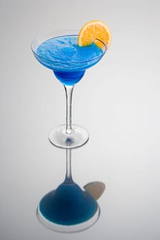 Frozen Blue Hawaiian mixed drink with orange slice garnish on grey background with reflection