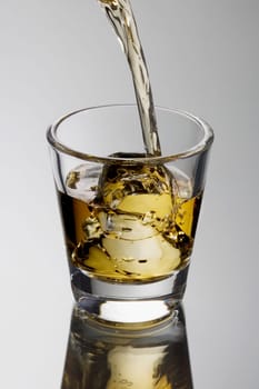 Scotch being poured on the rocks, on a grey background with reflection