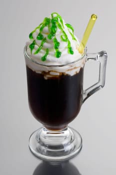 Irish Coffee mixed drink dressed up for St. Patrick's Day on grey background with reflection