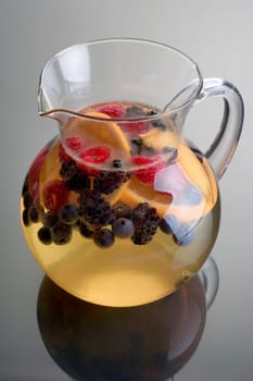 Pitcher of white wine sangria on grey background with reflection