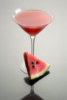 Watermelon Martini mixed drink with melon garnish on grey background with reflection