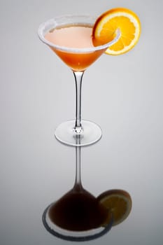 Sidecar mixed drink with orange garnish and sugar rim on plain grey background