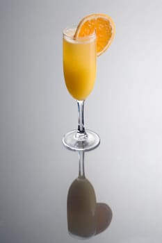 Mimosa mixed drink with orange slice garnish on grey background with reflection