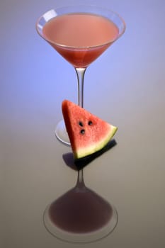 Watermelon Martini mixed drink with melon garnish on grey background with reflection