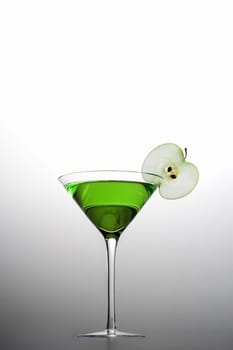 Apple Martini mixed drink with apple slice garnish on grey background