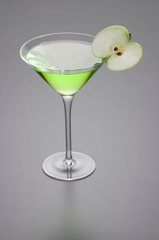 Apple Martini mixed drink with apple slice garnish on grey background