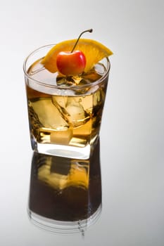Old Fashioned mixed drink with orange slice, cherry and sugar cube garnish on grey background with reflection