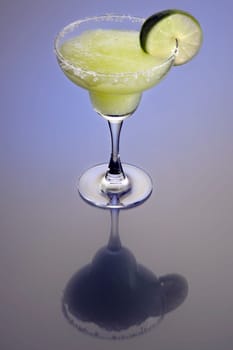 Frozen Margarita mixed drink with lime slice garnish on plain background with reflection