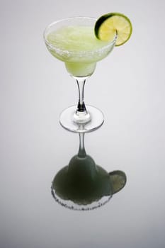 Frozen Margarita mixed drink with lime slice garnish on plain grey background with reflection