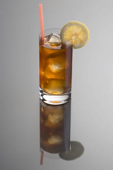 Long Island Ice Tea mixed drink with lemon slice garnish on grey background with reflection