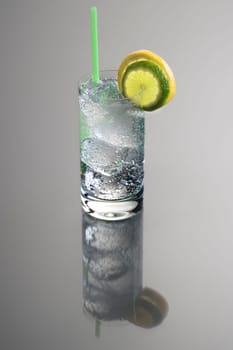 Vodka or Gin & Tonic mixed drink with lemon and lime slice garnish on grey background with reflection