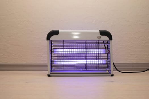 Electric Mosquito and Insect Zapper With Blue Purple Lights Turned on. Bug Killer Lamp on Wooden Floor in Room. Fly Trap for Outdoor and Indoor. Horizontal Plane . High quality photo