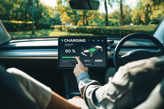 Electric car driver checks battery charging status, range and charging limit on app screen in the car. Smart technology device show EV car recharging data of electric storage in car battery innards.