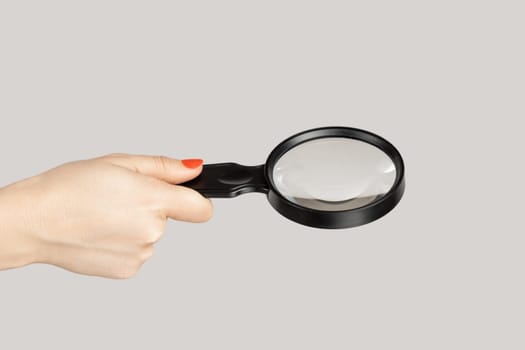 Closeup of woman hand showing loupe, magnificing glass, equipment for inspecting and zooming. Indoor studio shot isolated on gray background.
