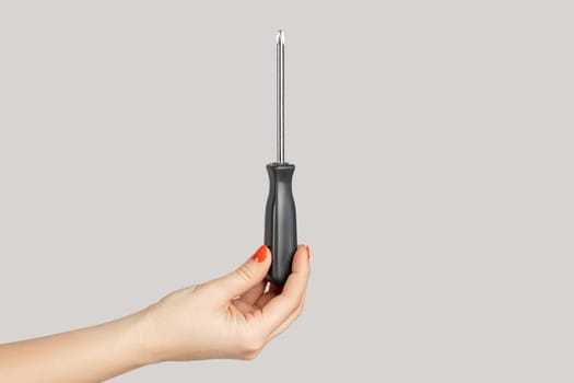 Closeup of woman hand showing black metal and plastic tool screwdriver for repair. Indoor studio shot isolated on gray background.