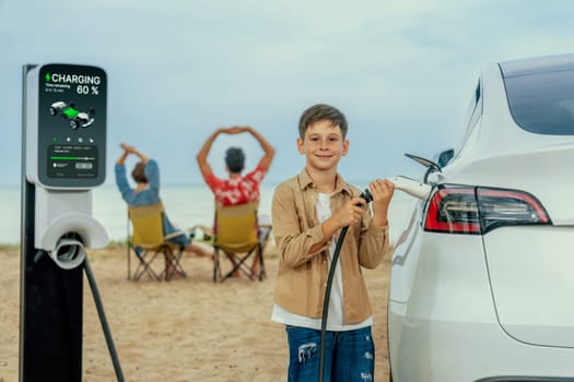 Family vacation trip traveling by the beach with electric car, little boy recharge EV car while his family enjoy seascape beach. Family trip with alternative energy and eco-friendly car. Perpetual