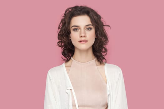 Portrait of beautiful charming winsome pretty woman with curly hair wearing casual style outfit looking at camera, being in good mood. Indoor studio shot isolated on pink background.