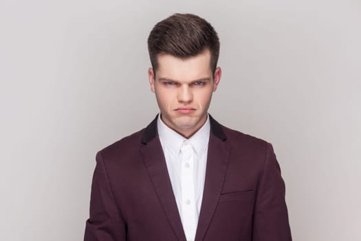 Portrait of gloomy sad handsome man has unhappy look, expresses regret and sadness, frowns face, being frustrated, wearing violet suit and white shirt. Indoor studio shot isolated on grey background.