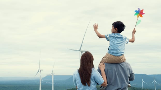 Concept of progressive happy family enjoying their time at the wind turbine farm. Electric generator from wind by wind turbine generator on the country side with hill and mountain on the horizon.