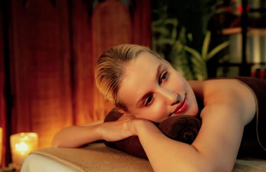 Caucasian woman customer enjoying relaxing anti-stress spa massage and pampering with beauty skin recreation leisure in warm candle lighting ambient salon spa at luxury resort or hotel. Quiescent