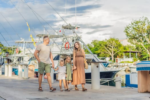 A happy, mature couple over 40 with their two daughters enjoying a leisurely walk on the waterfront, their joy evident as they embrace the journey of pregnancy later in life.