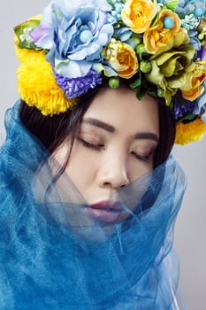 Portrait of sensual attractive woman with beautiful makeup , dark hair, with floral hat and blue veil, posing with closed eyes, expressing gentle. Indoor studio shot isolated on gray background,