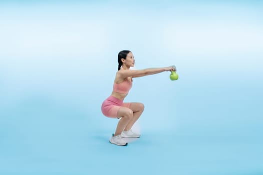 Vigorous energetic woman doing kettlebell weight lifting exercise on isolated background. Young athletic asian woman strength and endurance training session as body workout routine.