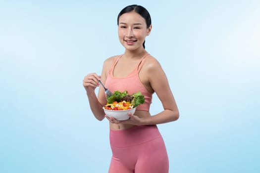 Young sporty Asian woman in sportswear holding salad bowl fill with vibrant of fruit and vegetable. Natural youthful and fit body lifestyle with balance nutrition on isolated background. Vigorous