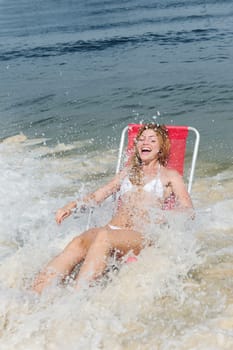 Woman in beach chair is surprised by wave