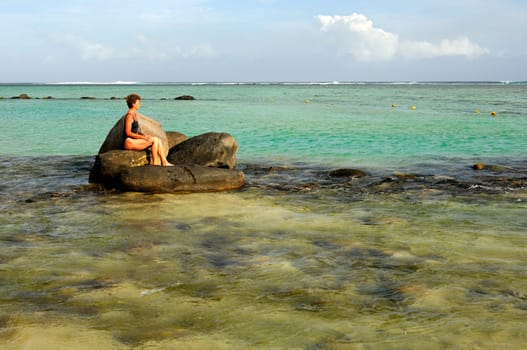 Woman sitting on a boulder in the turquoise waters of the Indian Ocean a
