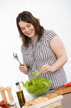 Cook - Plus size happy woman preparing salad in kitchen