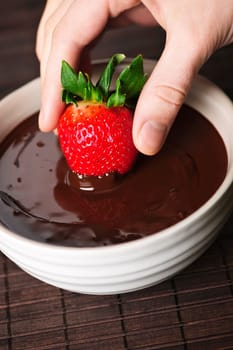 Hand dipping strawberry in chocolate