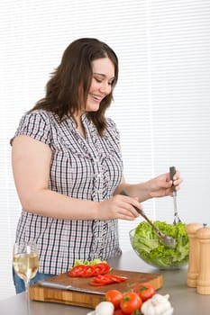 Cook - Plus size happy woman preparing salad in kitchen