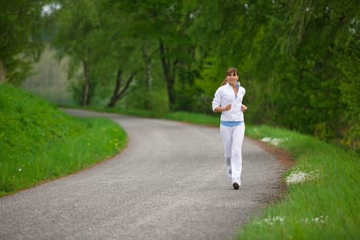 Jogging - sportive woman running on road in nature