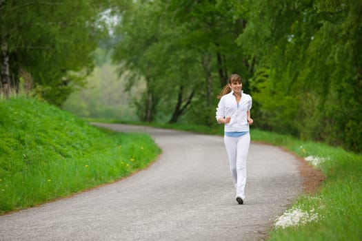 Jogging - sportive woman running on road in nature