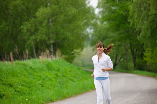 Jogging - sportive woman running on road in nature