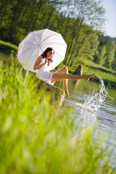 Happy romantic woman sitting by lake splashing water