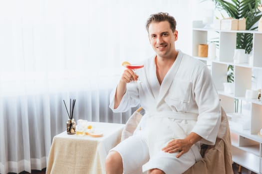 Beauty or body treatment spa salon vacation lifestyle concept with man wearing bathrobe relaxing with drinks in luxurious hotel spa or resort room. Vacation and leisure relaxation. Quiescent