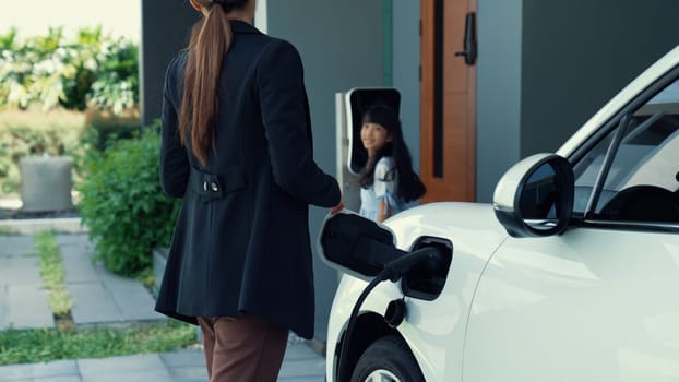 Progressive lifestyle of mother and daughter who have just returned from school in an electric vehicle that is being charged at home. Electric vehicle powered by sustainable clean energy.