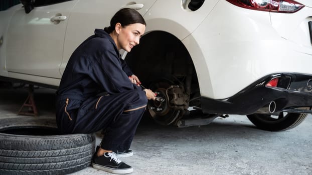 Hardworking female mechanic changing car wheel in auto repair workshop. Automotive service worker changing leaking rubber tire in concept of professional car care and maintenance. Oxus