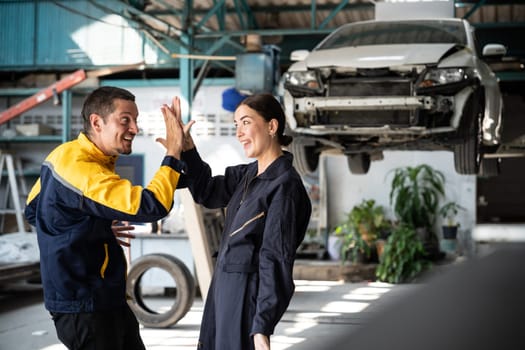 Two happy vehicle mechanic celebrate and high five after made successful car inspection or repair in automotive service car workshop. Technician team enjoy accomplishment together in garage. Oxus