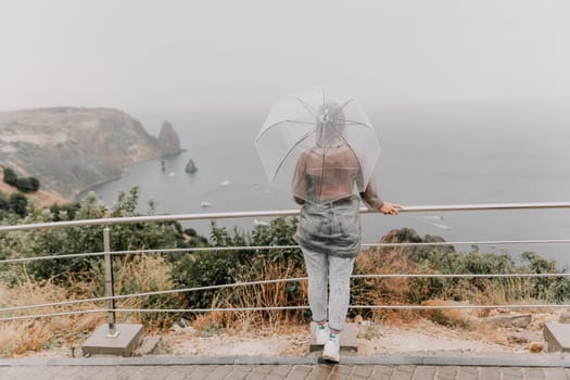 Woman rain park. Happy woman portrait wearing a raincoat with transparent umbrella outdoors on rainy day in park near sea. Girl on the nature on rainy overcast day