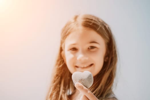 Female hand holding a stone in the shape of a heart against the background of the sea